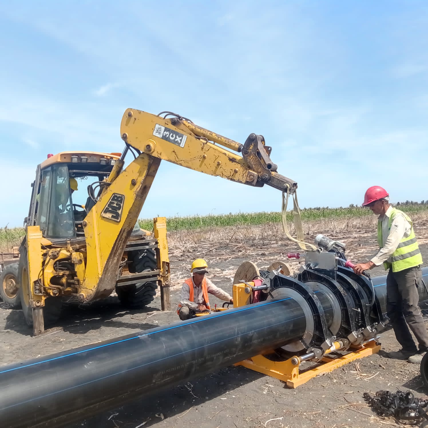 Workers installing large pipe with construction equipment